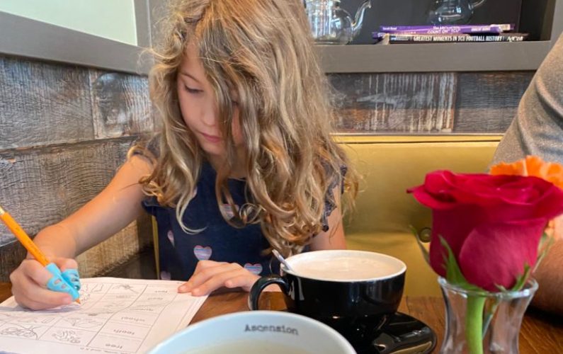 young girl doing homework at table with coffee